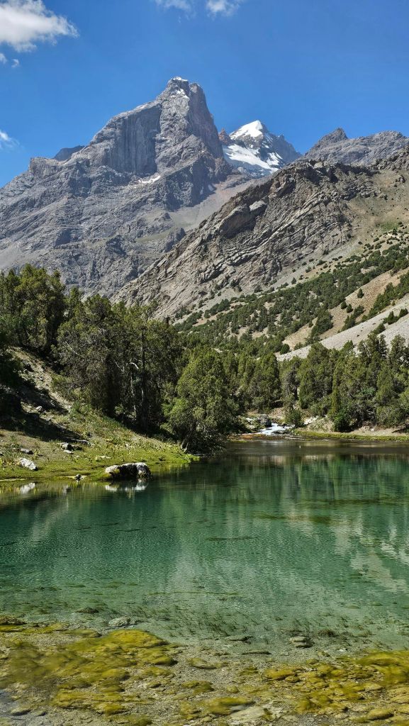 malé Alaudinské jazero ktoré má tyrkisovú farbu. Navôkol tujový les a zasnežené hory.