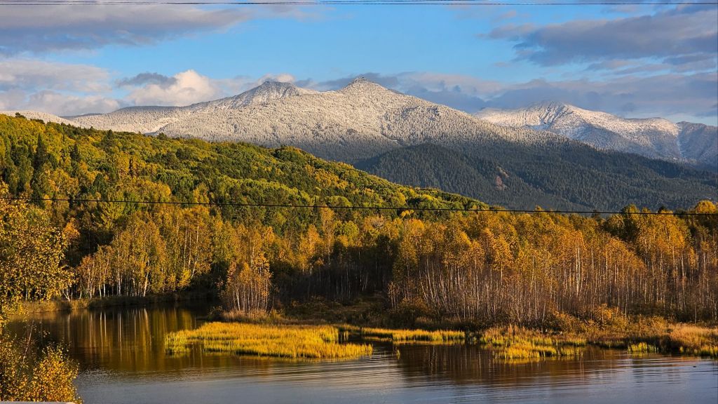 Jeseň na ruskej sibíri. jazero, brezy zafarbené do jesenných farieb, v pozadí prvý sneh na horách.
