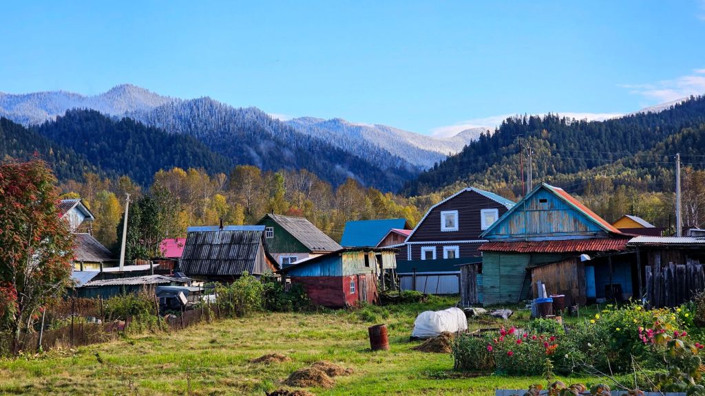 Ruská dedinka počas jesene. farebné drevené domčeky s okenicami, záhrada a v pozadí už zasnežené kopce. sibír.