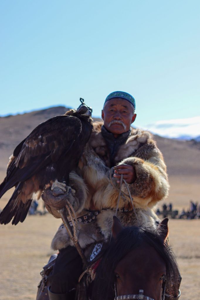 festival orlích lovcov a ujo mongol alebo kazach na koni v tradičnom kožuchu s orlom na ruke