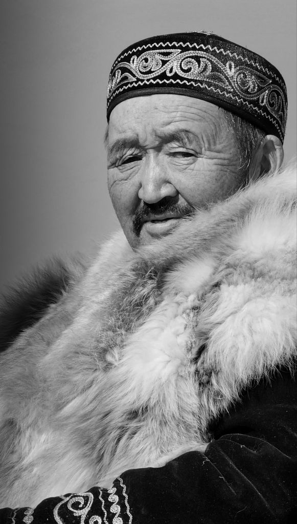 starší Mongol ktorý má vrásky na tvári a na hlave tradičnú čiapku so vzorom a líščí kožuch