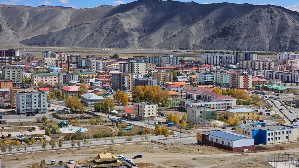 mestská štvrť, škola parky, budovy a paneláky uprostred stepi a v pozadí obrovské hory