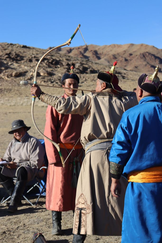 mongol lukostrelec strieľajúci lukom do terča na festivale. oblečený v tradičnom oblečení a s čiapkov s anténou