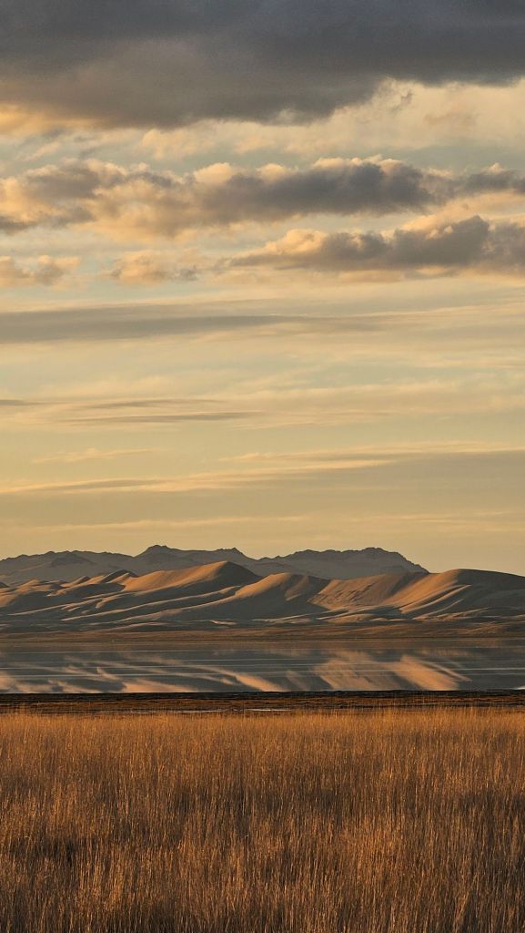 piesočné duny ktoré sú ožiarené slnečným svetlom pri západe slnka ktoré sa odrážaju na hladine jazera v mongolsku